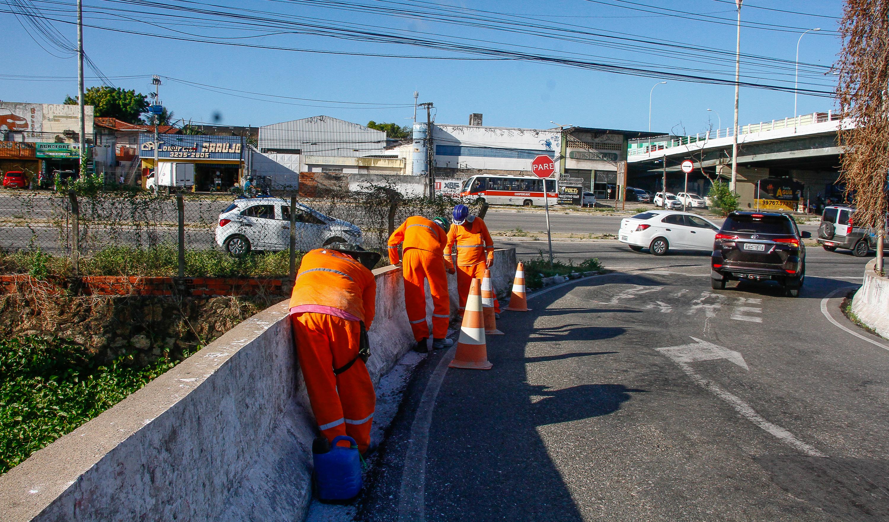 três operários trabalhando em guarda-corpo de viaduto e carros passando ao fundo